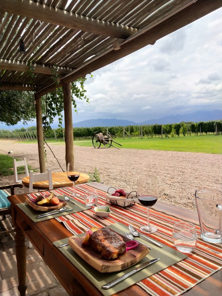 A table with two glasses of red wine, and two board with meat and vegetables