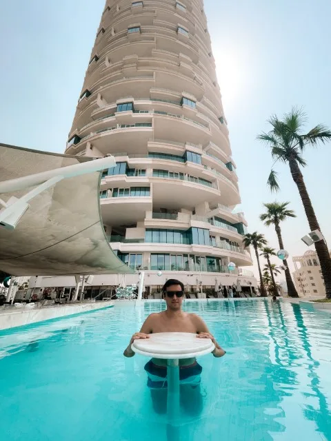 A man in a swimming pool with a tall building in hte back