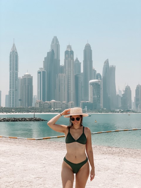 A woman in a bikini standing on a beach with Dubai's city skyline in the background