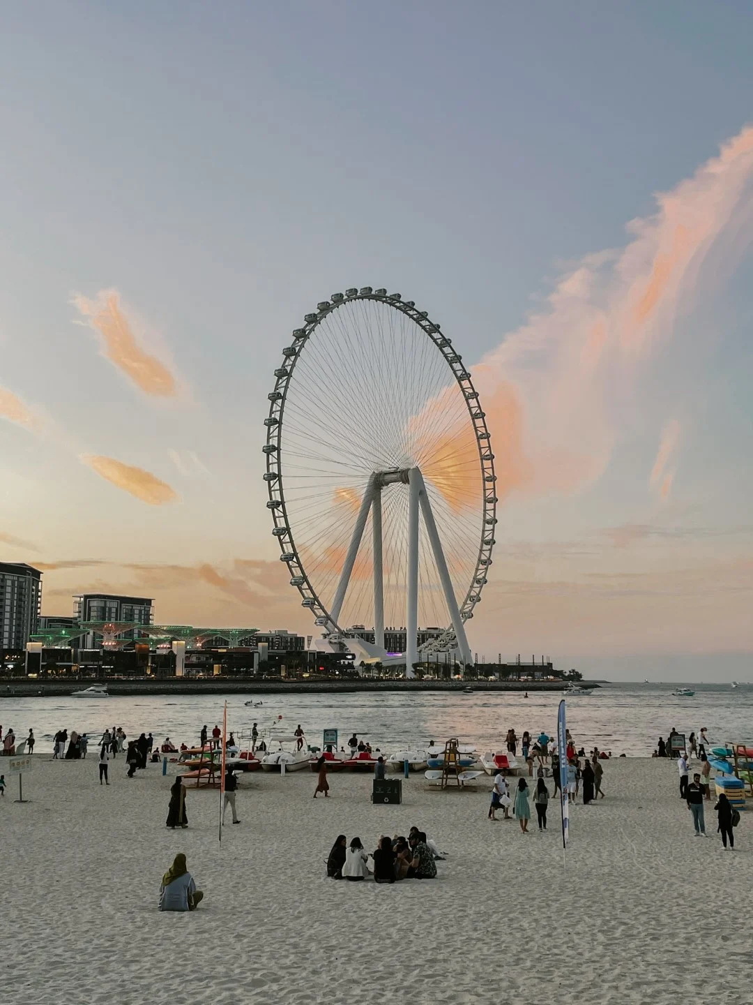 A beach with people, and a massive ferris wheel in the background