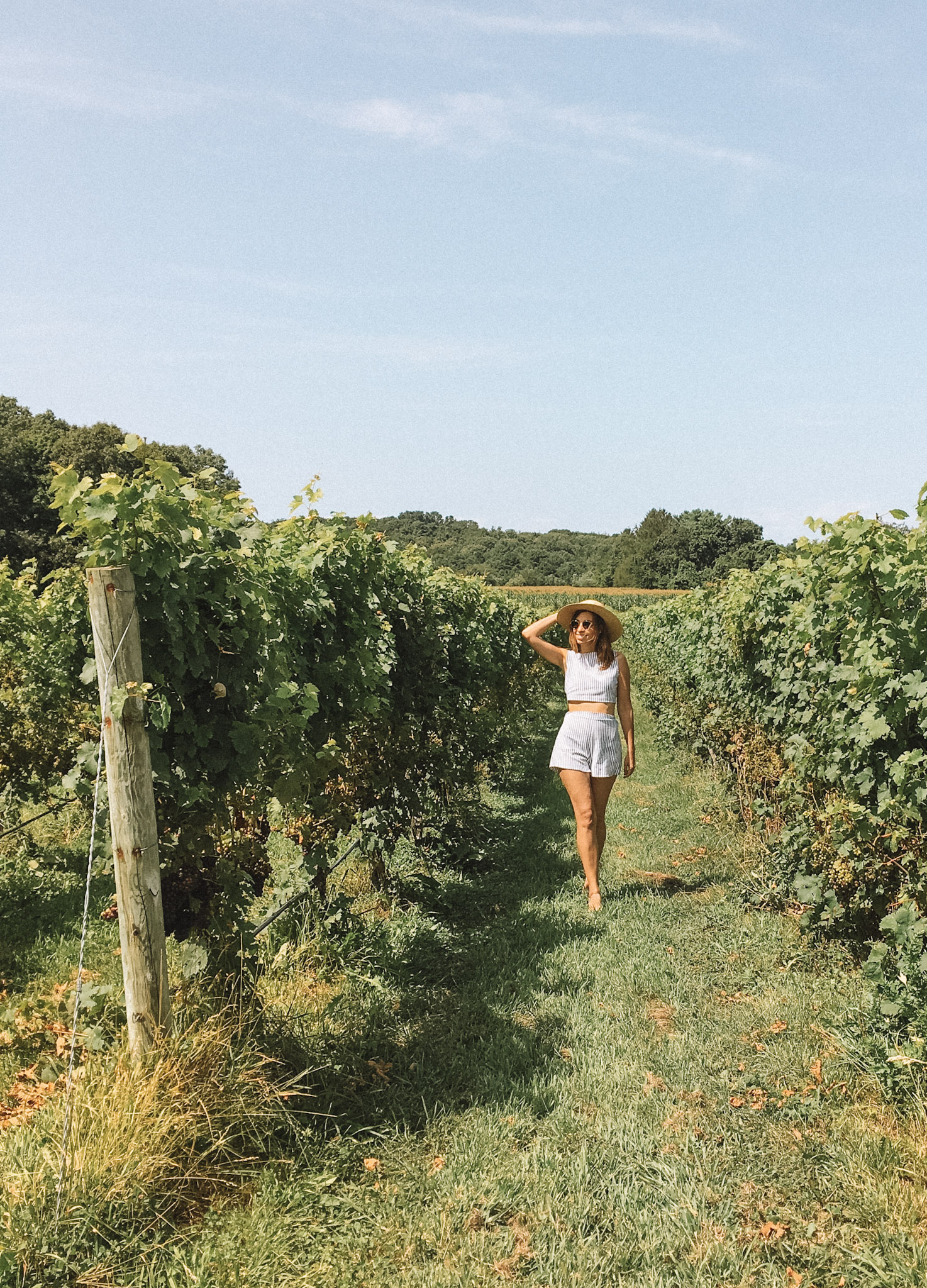 Image of a woman smiling between two  vineyard rows while visiting a winery, one of the best things to do in Long Island. 