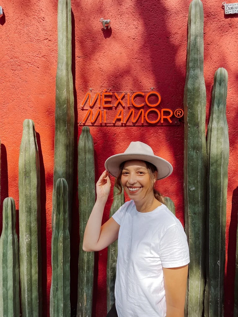 A woman smiling in front of a red wall with the sign Mexico Mi Amor, in Polanco