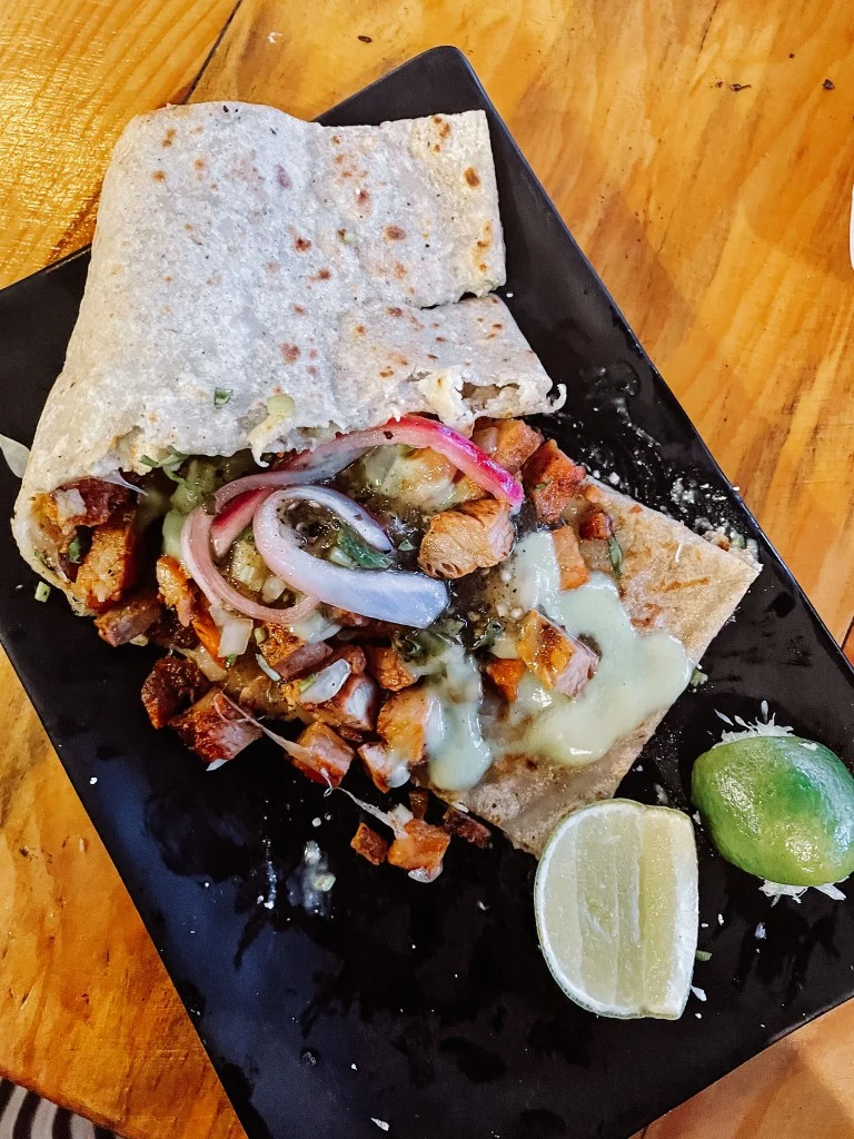 A Mexican tortilla with fillings set on a black plate, and two lime wedges on the side