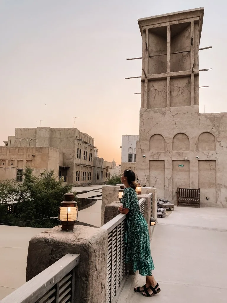 A woman leaning on a wall in Al Seef, with traditional buildings in the background