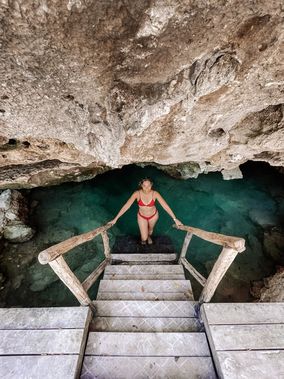 Woman in bikini standing at the end of a staircase down a cenote in Tulum.