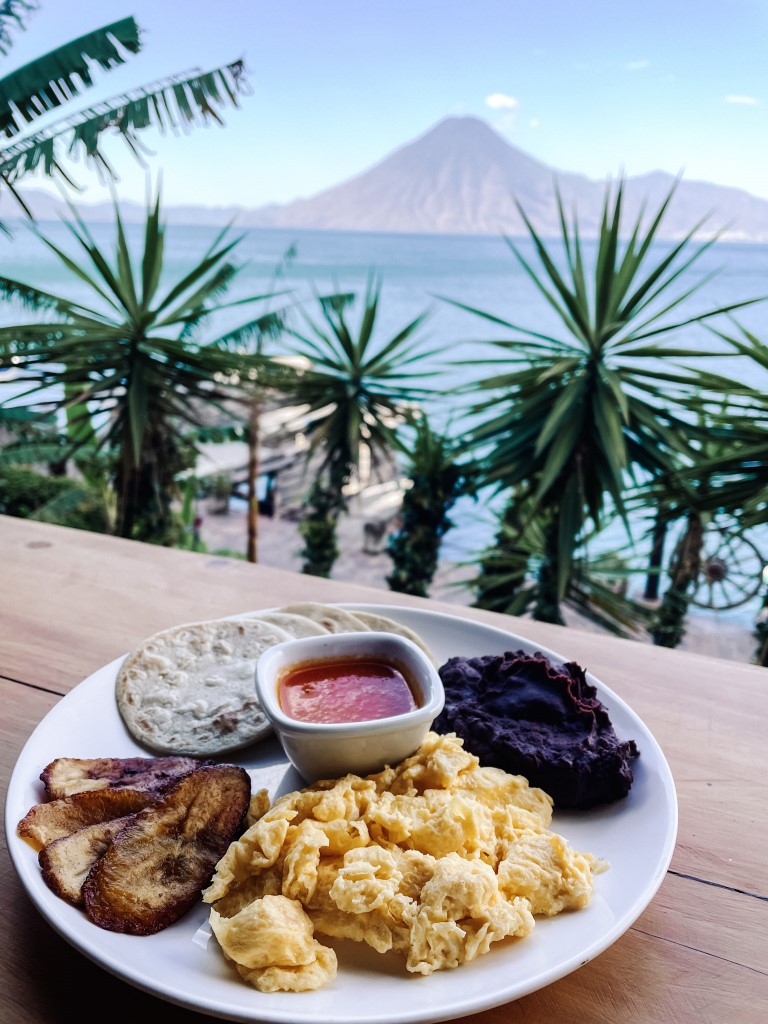 A breakfast plate on the forefront, and a lake and volcanoes in the background