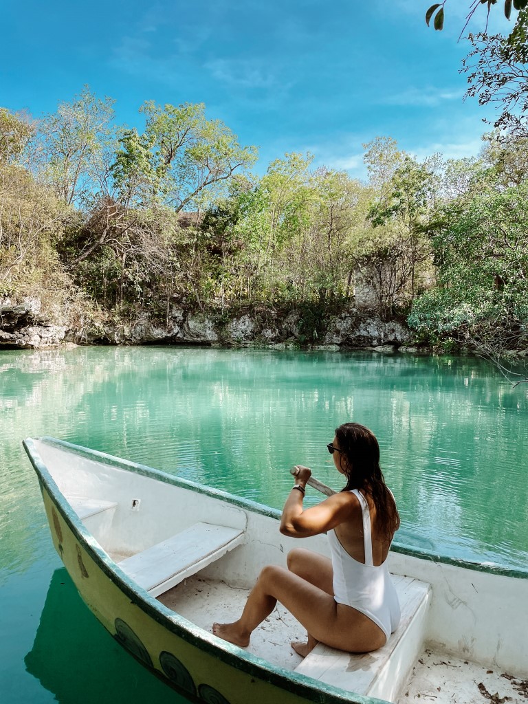 A woman in a white swimsuit paddling on a boat in an open cenote