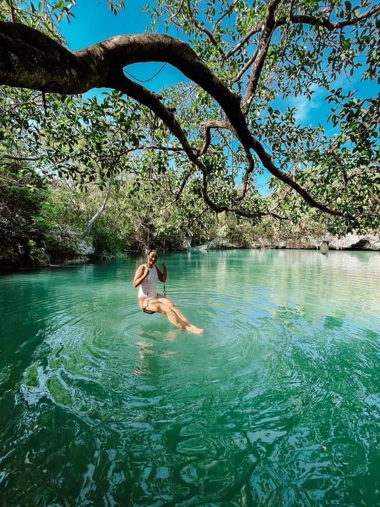 A woman looking at the camera while sitting on a swing in an open cenote.