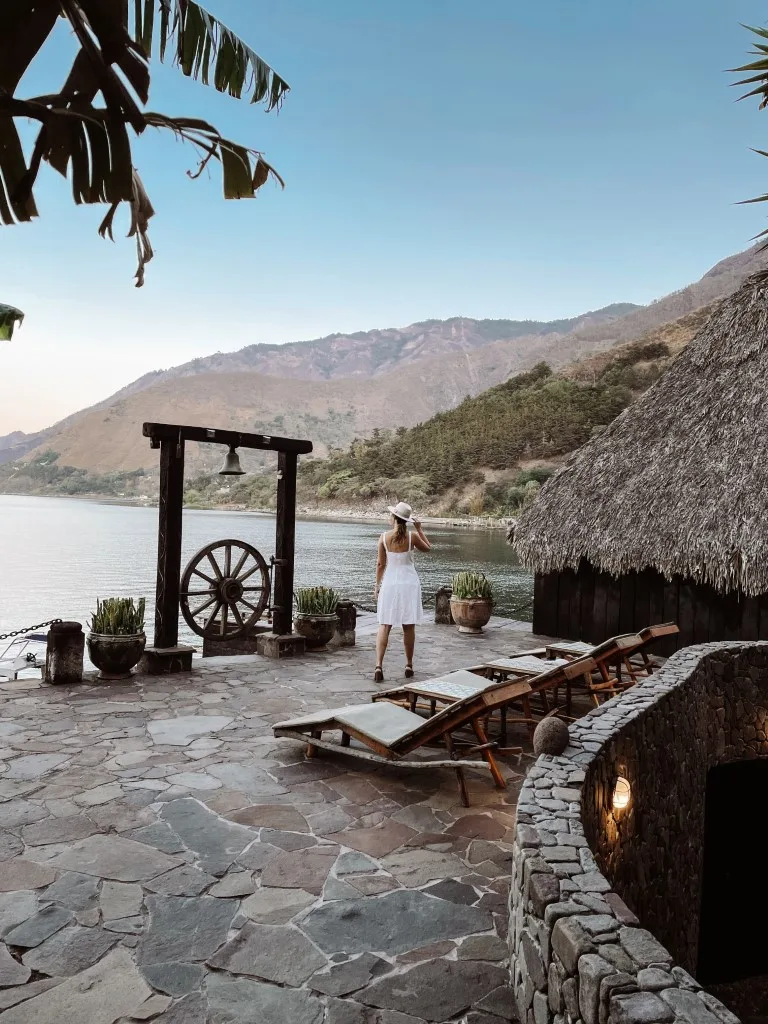 A woman in a white dress walking on the lake-shore property of a hotel