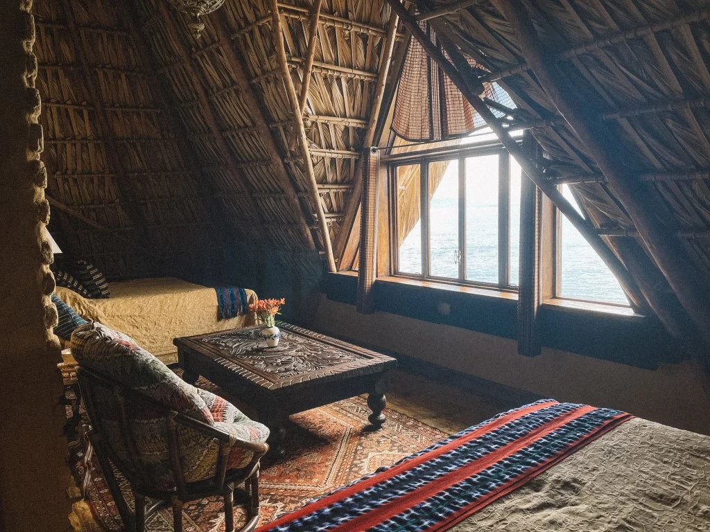 The interior of a rustic hotel room with a big window that opens to a lake