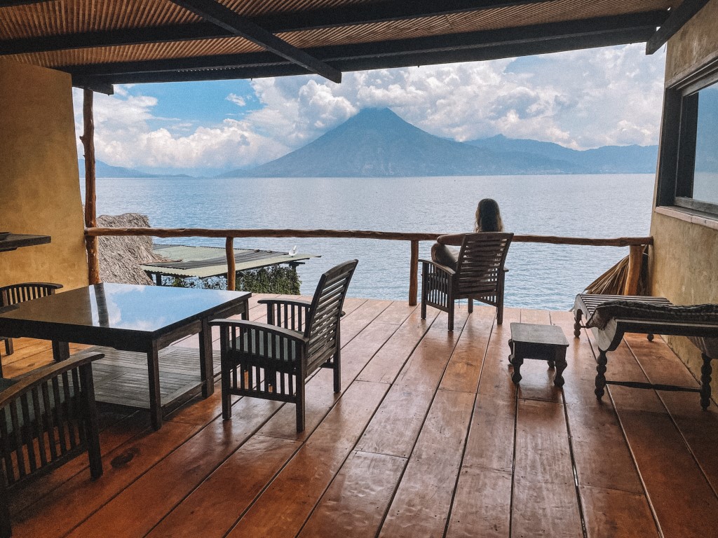 A woman sitting on a chai in a spacious deck overlooking a lake and volcanoes in the background