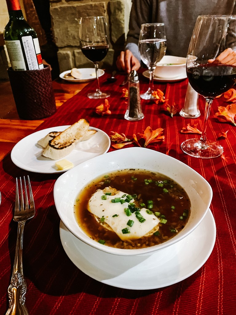 A dinner plate, two glasses of wine, and a plate with bread in a table with a red tablecloth