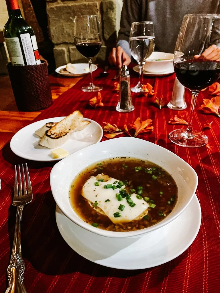 A dinner plate, two glasses of wine, and a plate with bread in a table with a red tablecloth