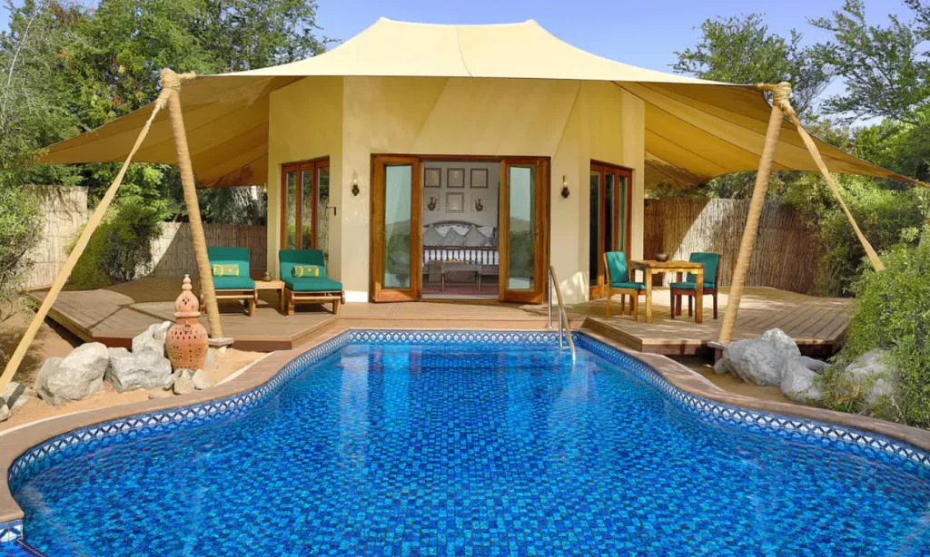 A luxurious yellow tent surrounded by a wooden deck with sun loungers, and a large swimming pool.