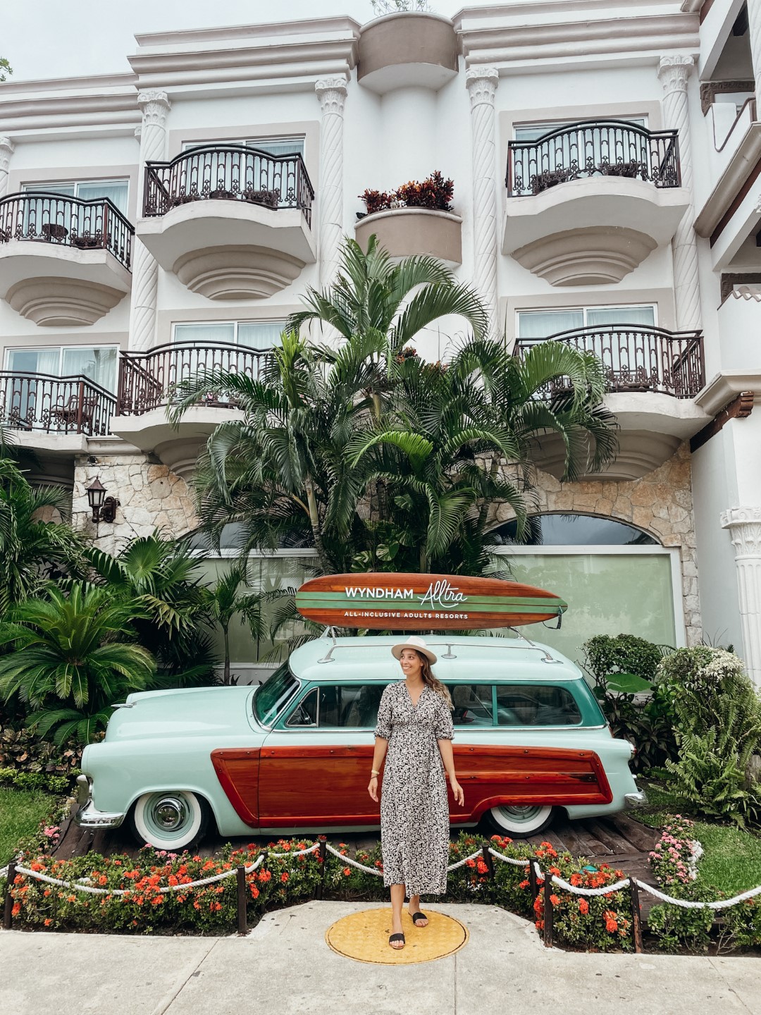 A woman standing in front of a vintage car placed in front of an elegant building