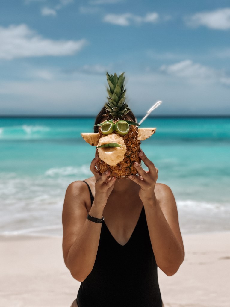 A woman holding a pineapple in the shape of a monkey face, covering her own face with it 