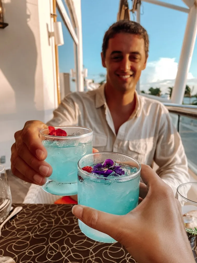 A man holding a glass with a blue drink,  and a woman's hand holding an identical drink