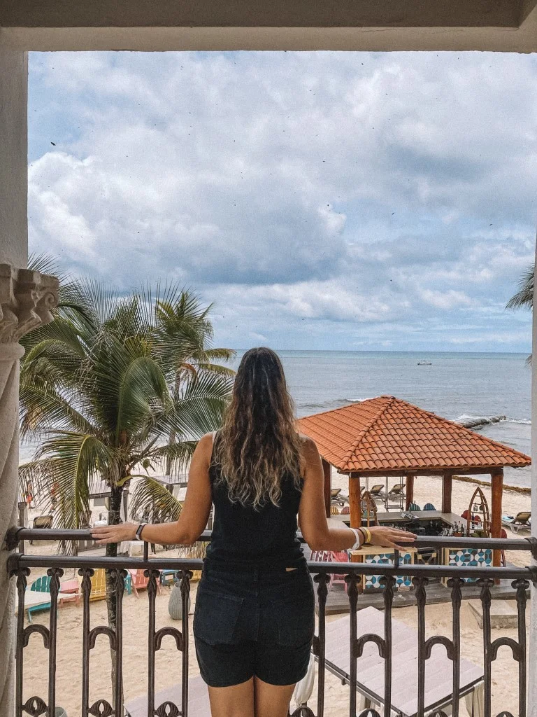 A woman standing in a balcony, overlooking the beach 