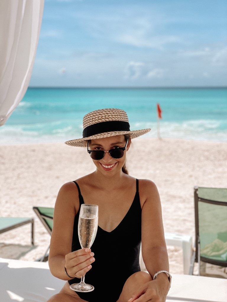 A woman sitting on a beach bed and holding a champagne flute, inserted in a post about a Cancun itinerary 