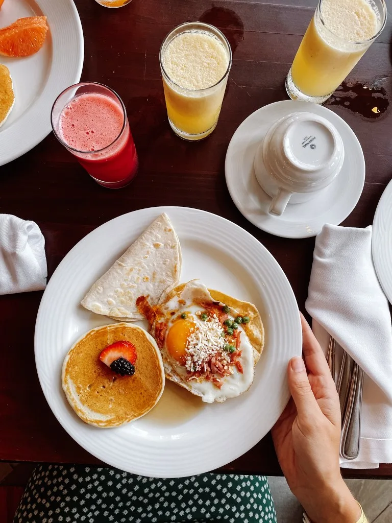 A pancake, fried egg, and bread in a white plate, and three glasses of juice set on a table