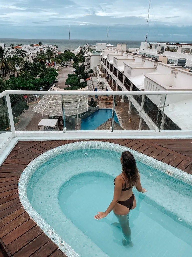 A woman in a rooftop hot tub overlooking the hotel's property and the beach in the distance