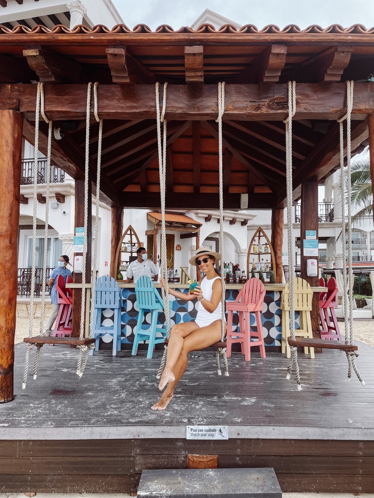 A woman in a white swimsuit, sitting on a swing in a beach bar 