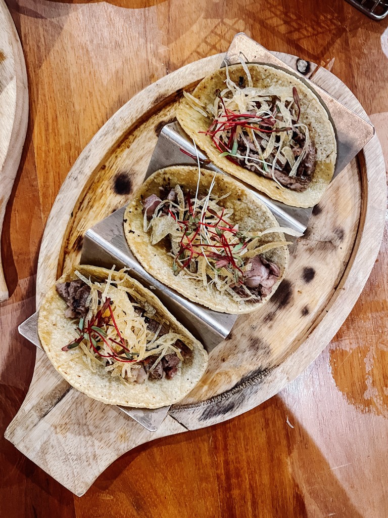 A wooden board with three tasty-looking tacos in a restaurant 