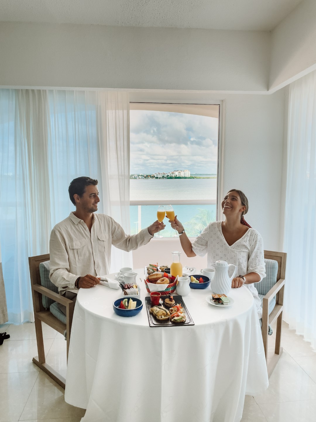 A couple having breakfast in the room at Wyndham Alltra Cancun, with a window overlooking the sea in the background