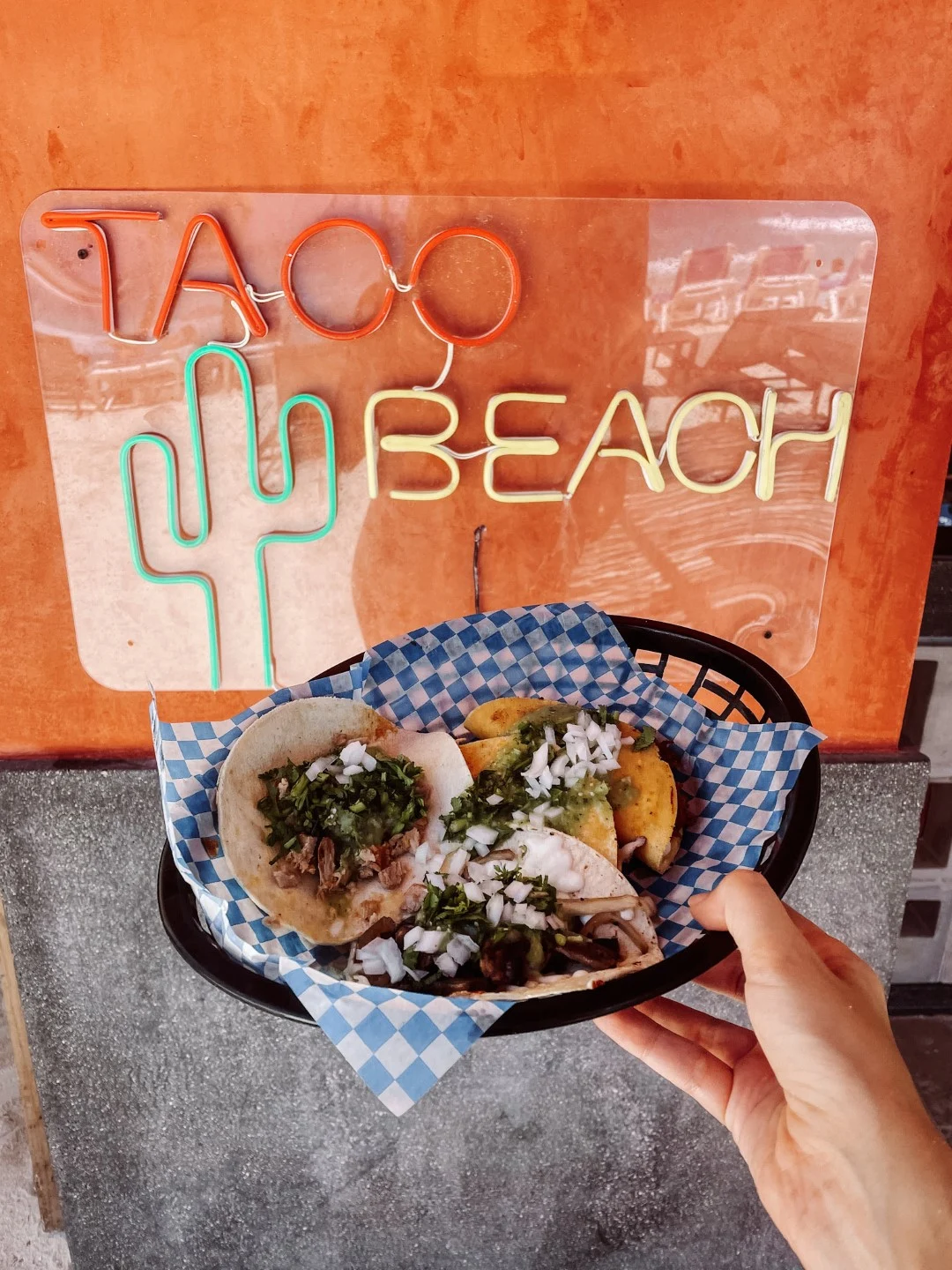 A basket of tacos photographed against a red wall with a sign that reads Taco Beach