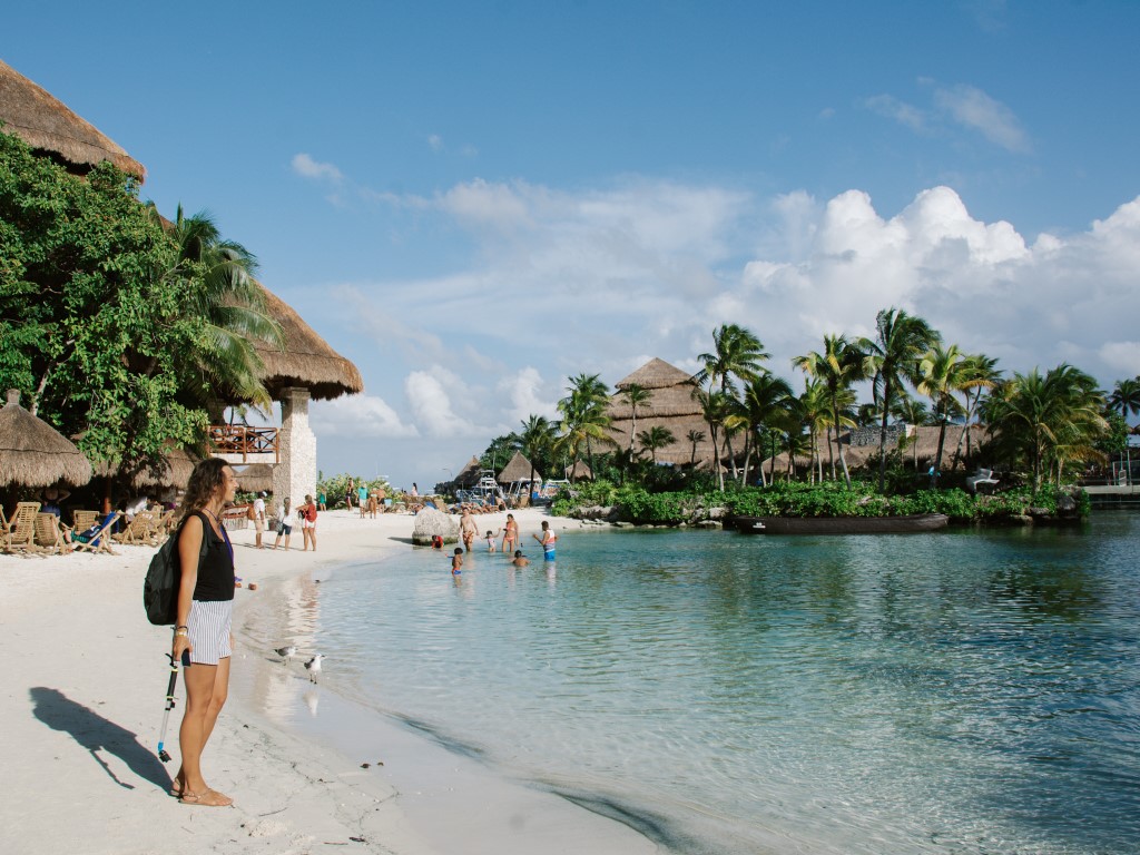 A woman standing on the shore of a beach, holding a snorkel hear, with palm trees in the background. Inserted in a post about the ideal Cancun itinerary 