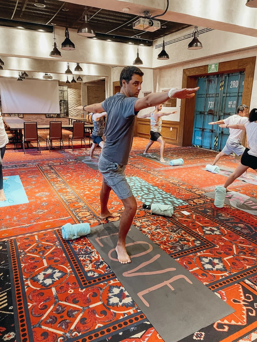 A man practicing yoga at a yoga class, with other students in the background