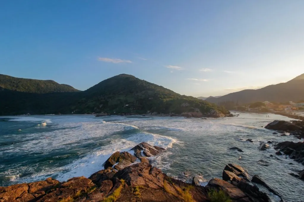 A beach with rocky outcrops and hills in the background