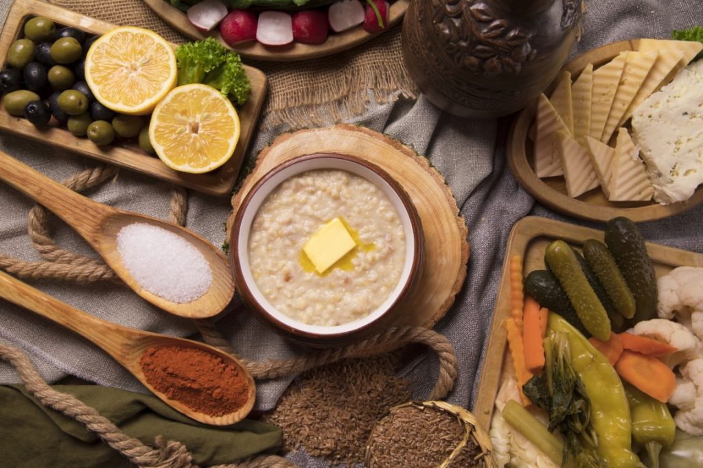 An overhead shot of a table with a bowl of Harees, pickled vegetables, cheeses, olives, and spices