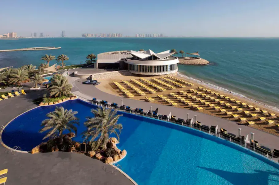 A large swimming pool, and a beach area filled with yellow sunbeds in the background