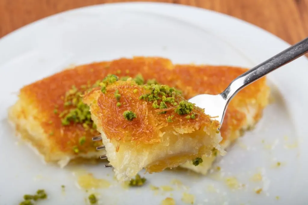 a fork holding a piece of Kunafa over a plate