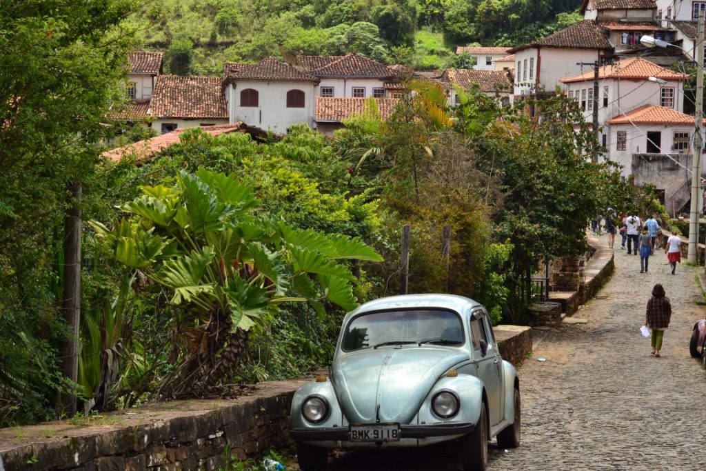 A beetle car parked in a narrow cobblestoned street with vegetation in the background