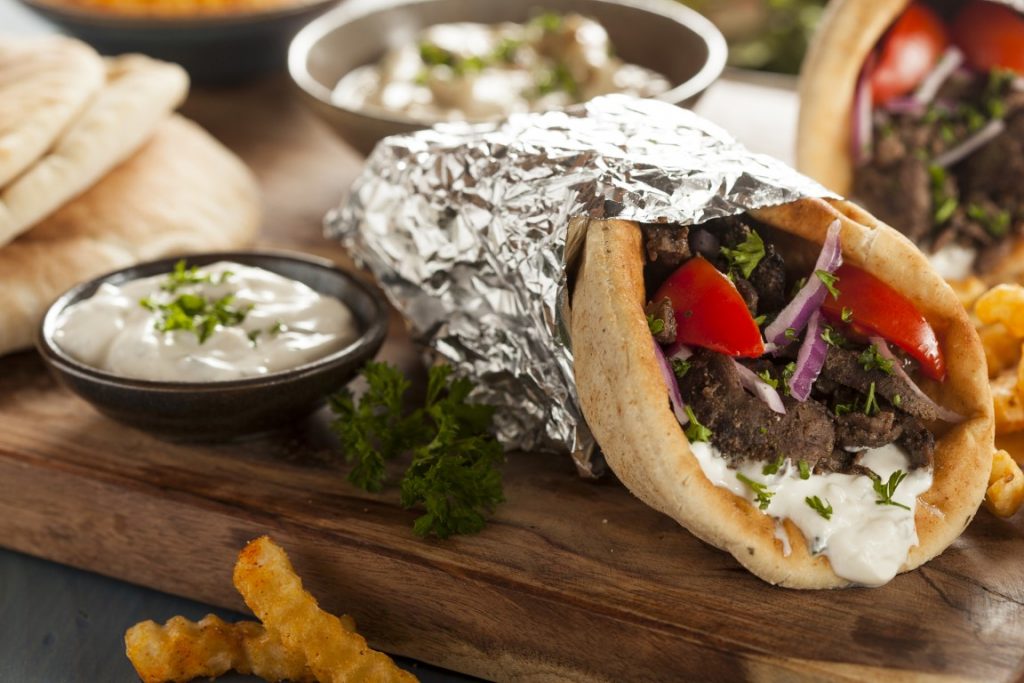 Shawarma wrapped in kitchen foil paper with a dip on the side