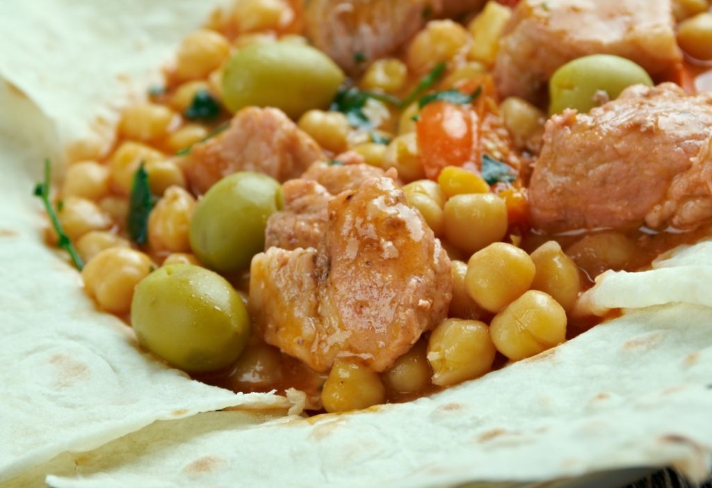 A close-up image of a stew with meat, chickpeas, and olives