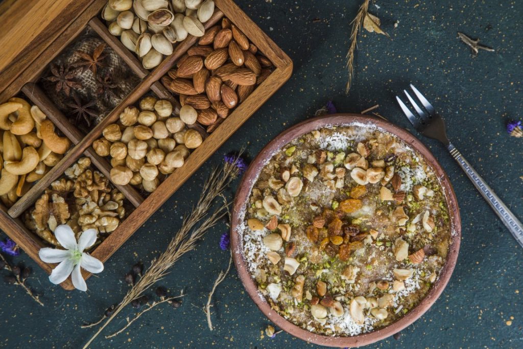 A bowl with umm ali dessert, and a wooden box filled with nuts to the side