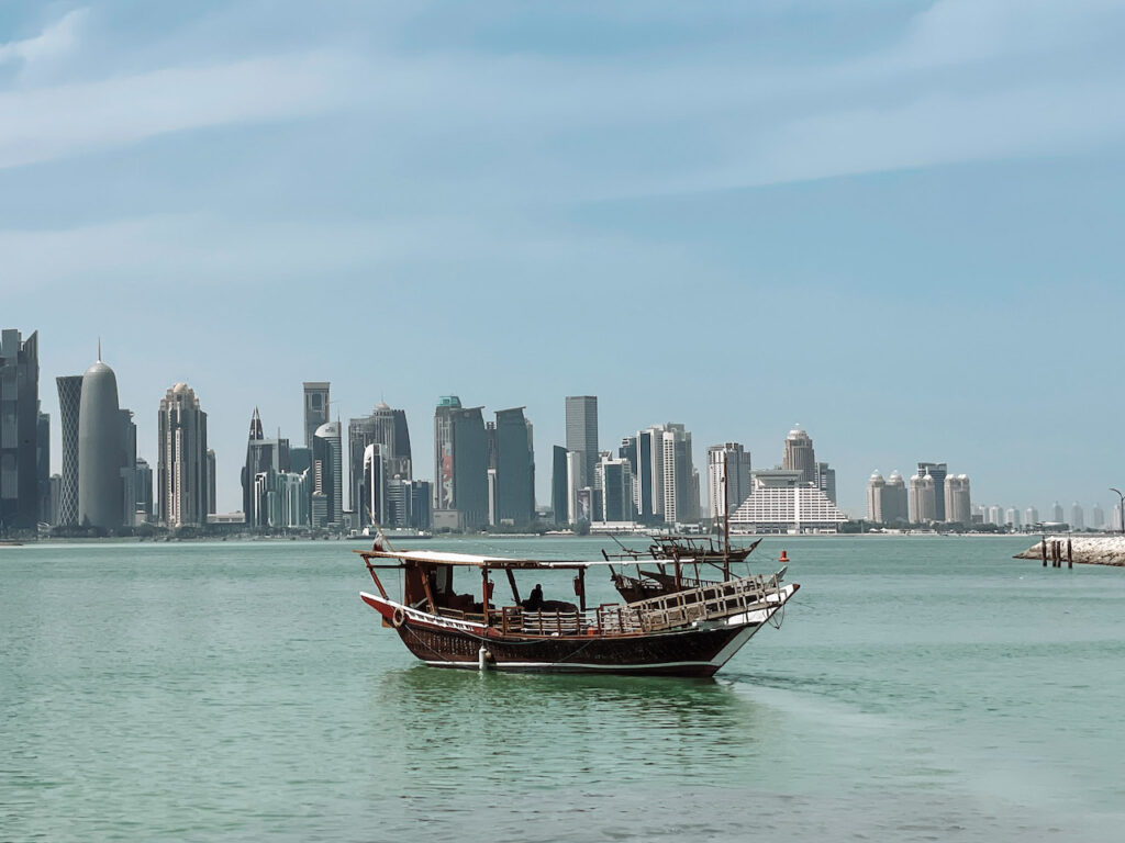 A dhow boat in the water, and skyscrapers in the background