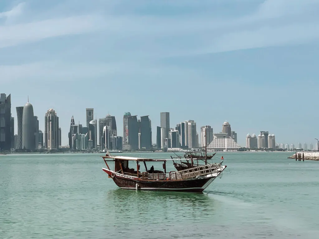 A dhow boat in the water, and skyscrapers in the background