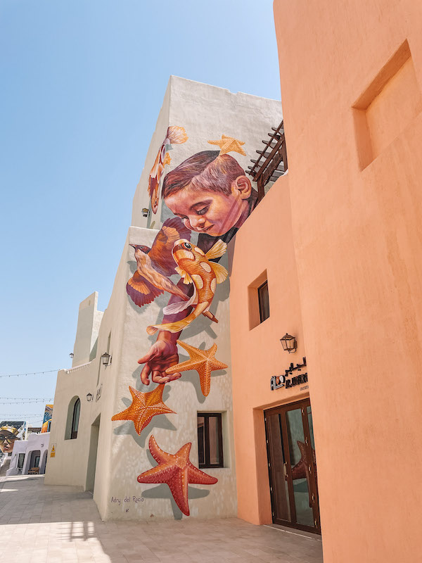 A colorful mural of a boy playing with an orange fish and starfish on the side of a building