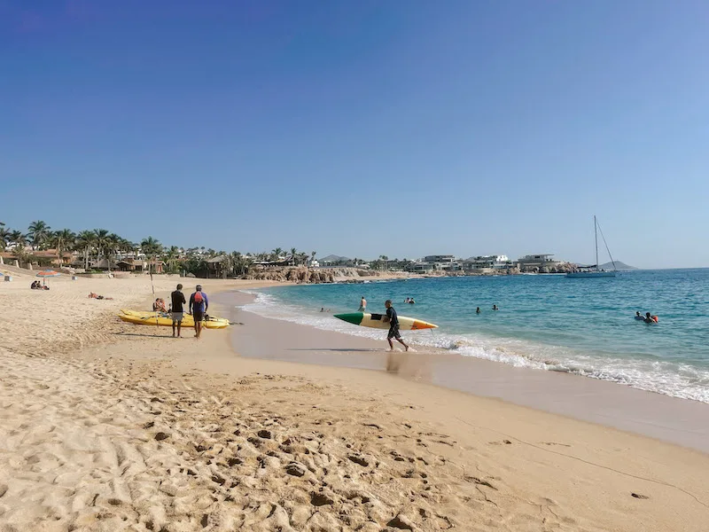 A surfer walking out of the water in a beach in Los Cabos 