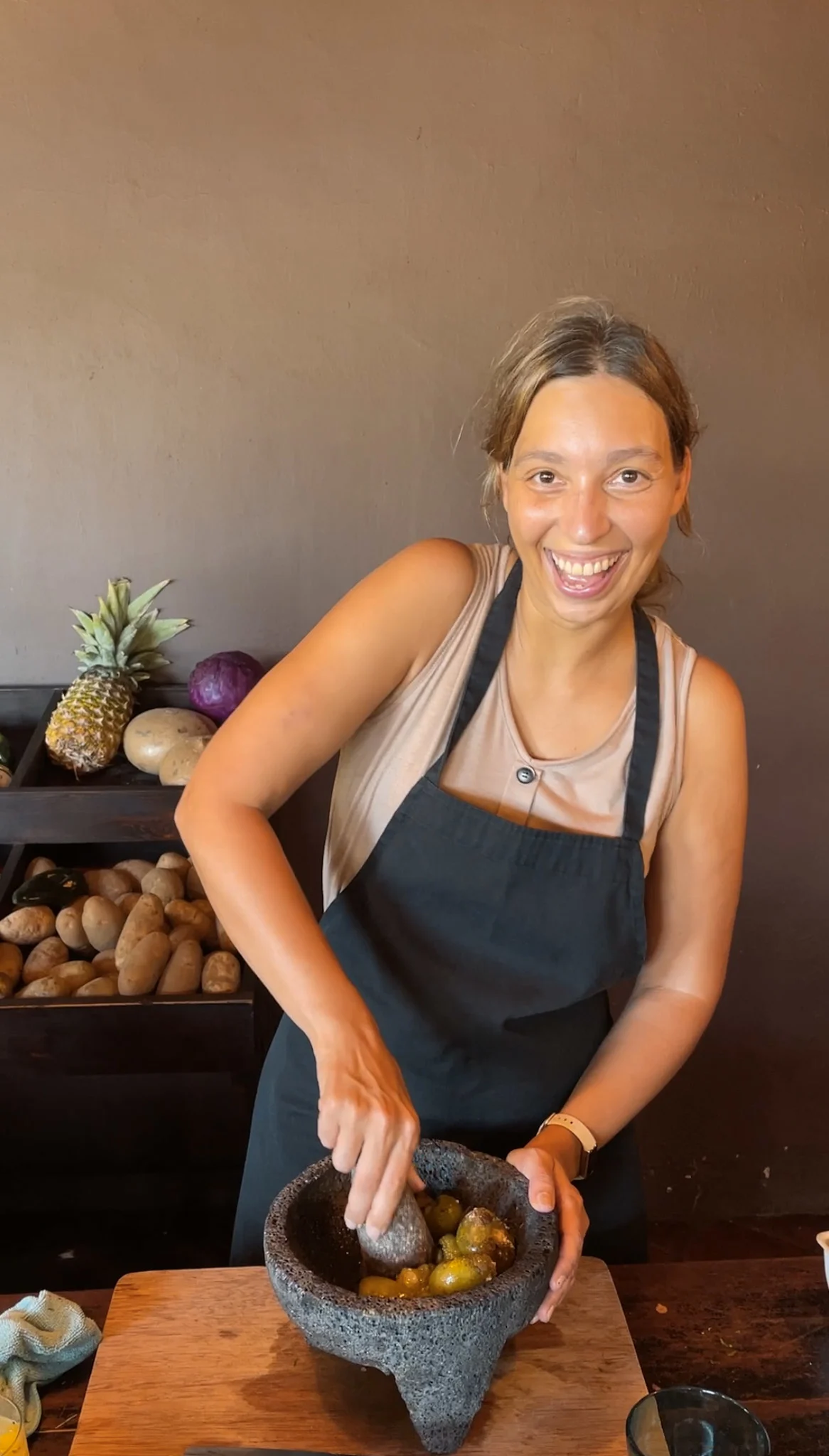 A woman smiling as she grinds ingredients in a mortar and pestle during a cooking class