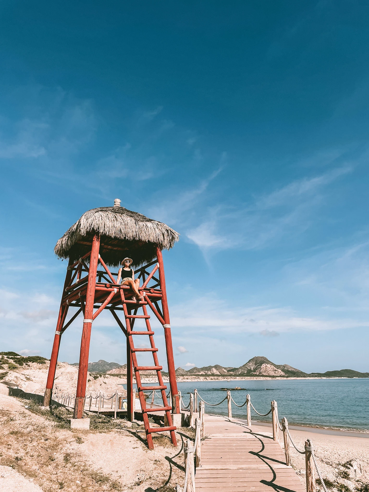 A red beach tower in Cabo Pulmo, with a woman sitting at the top