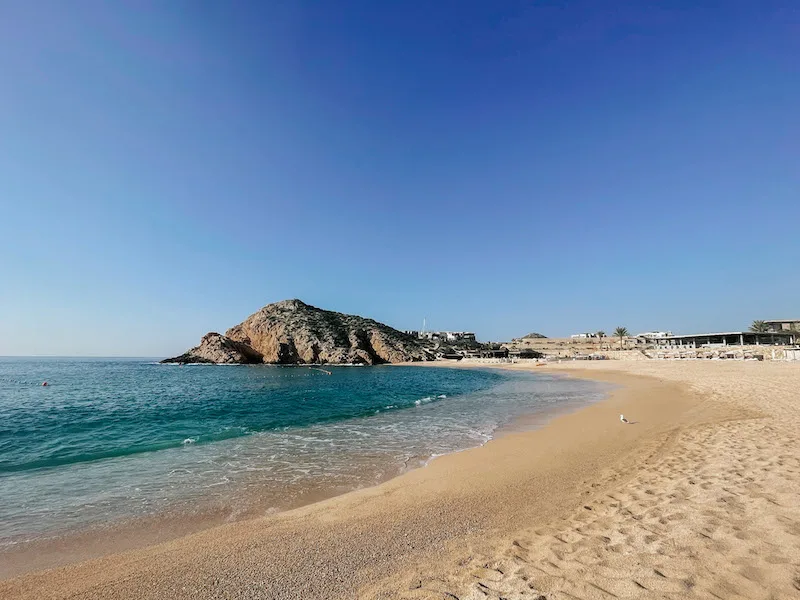 A golden-sand beach with blue waters, and a rock formation in the background