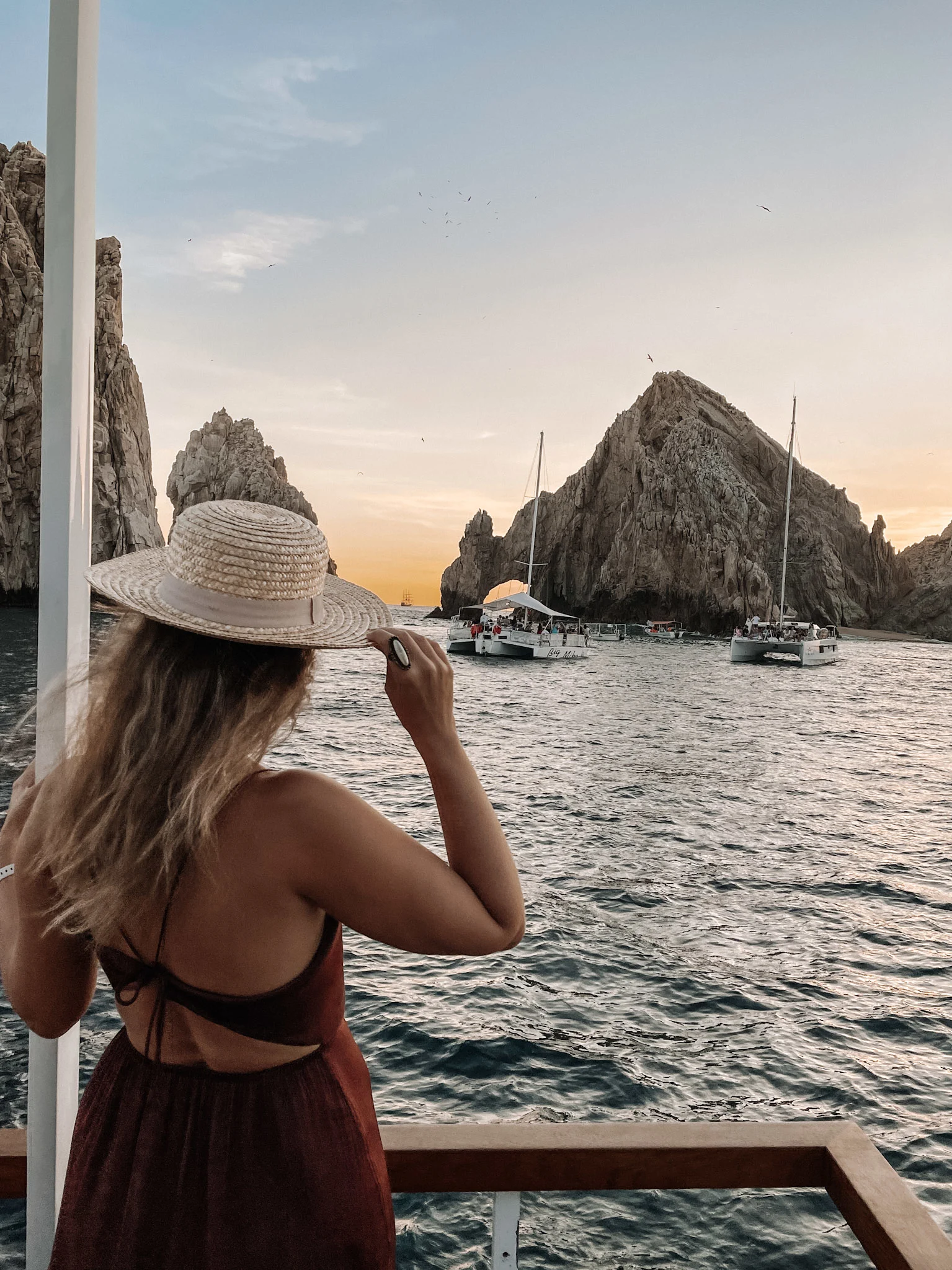 A woman on a cruise in Los Cabos, overlooking the rock formations on the water, and other boats