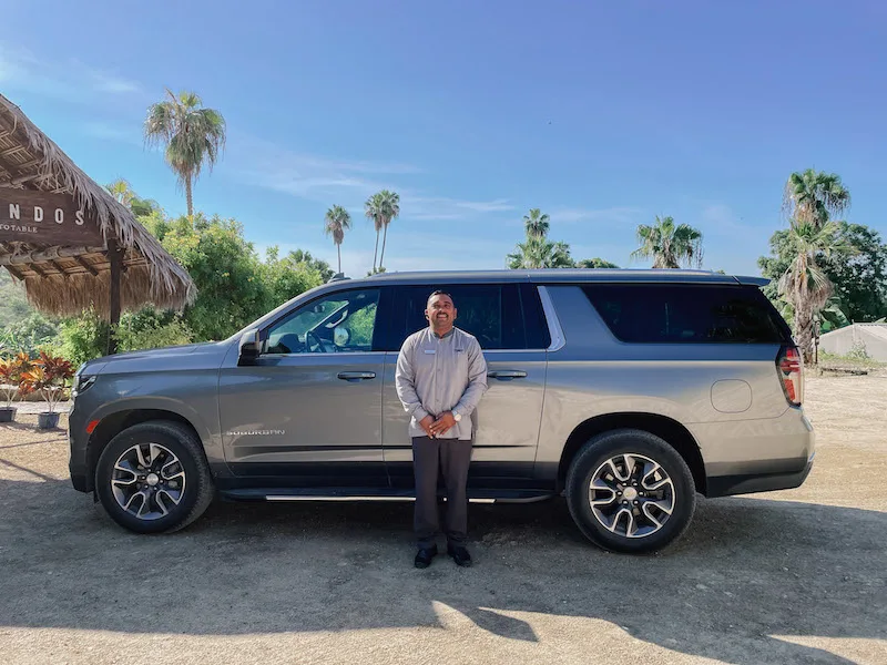 A smiling private driver standing in front of a luxurious vehicle