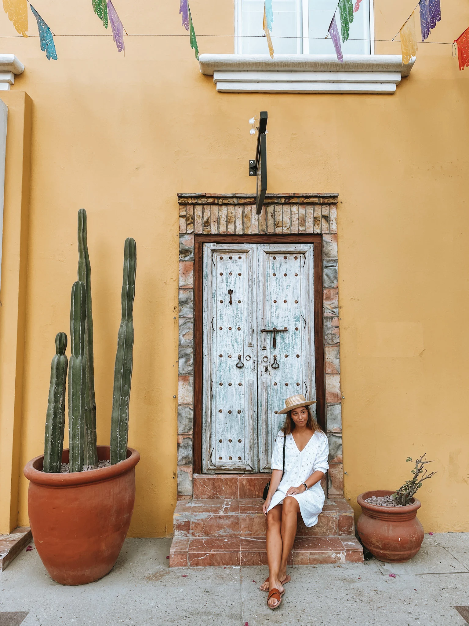 A woman seating on the steps in front of an old-looking door and a yellow wall