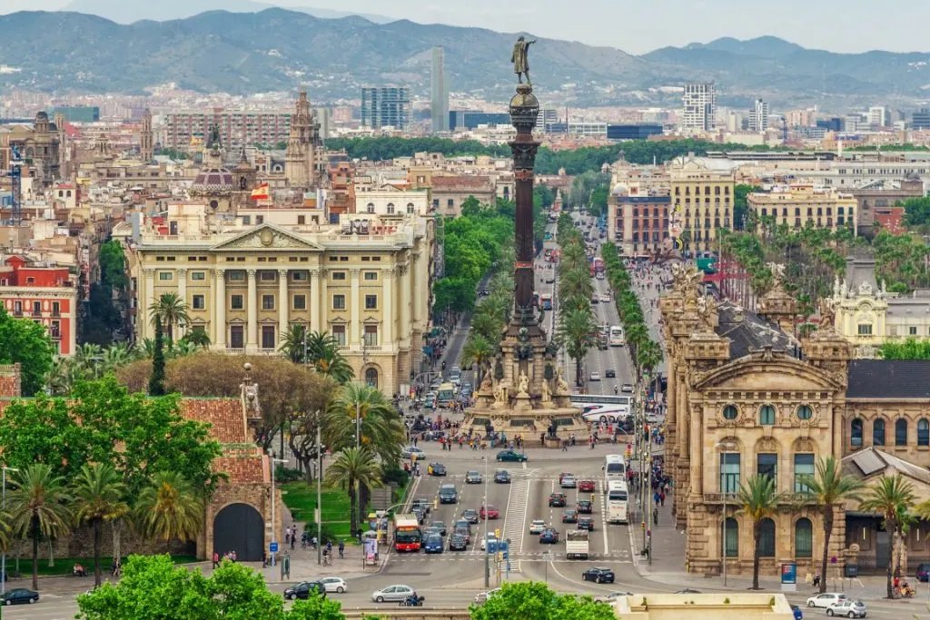 Image of Barcelona from above, featuring a street in the center lined by palm trees and buildings, and the Columbus Monument in the middle, inserted in a post about the best Barcelona Tours. 